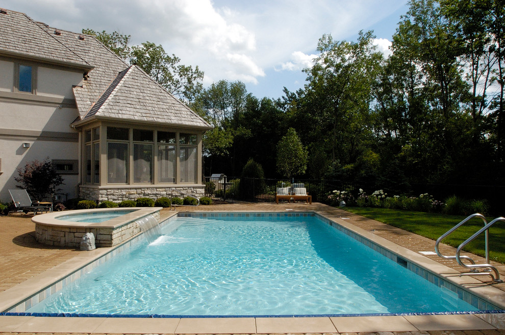 Modelo de piscinas y jacuzzis alargados clásicos de tamaño medio rectangulares en patio trasero con adoquines de hormigón