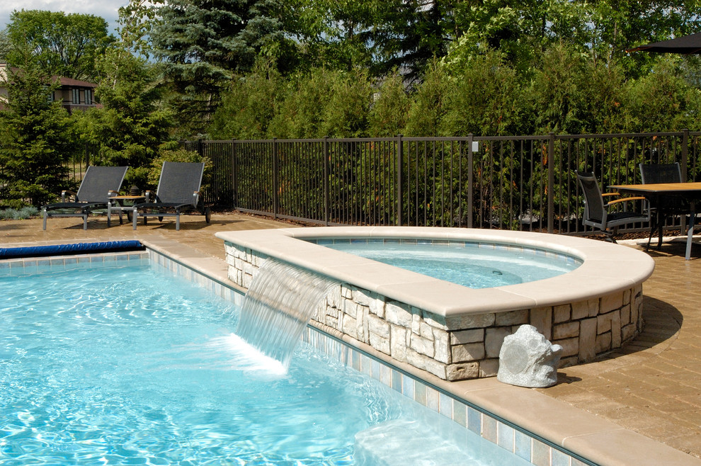 Ejemplo de piscinas y jacuzzis alargados tradicionales de tamaño medio rectangulares en patio trasero con adoquines de hormigón