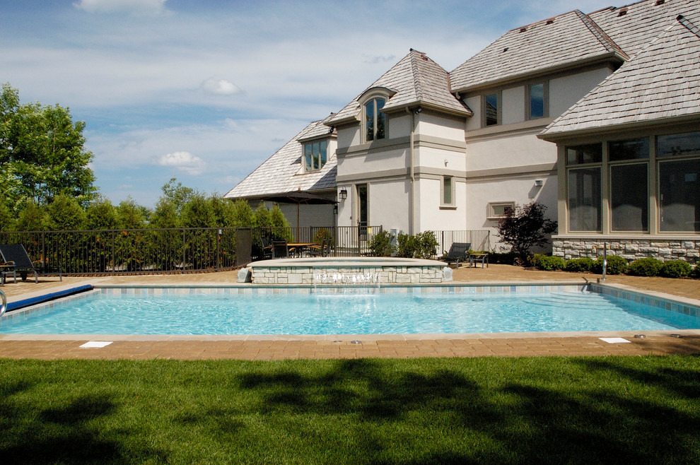 Modelo de piscinas y jacuzzis alargados clásicos de tamaño medio rectangulares en patio trasero con adoquines de hormigón