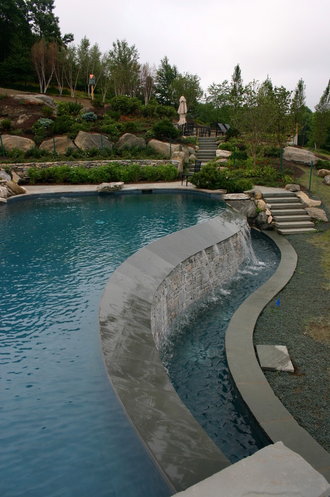Cette image montre une grande piscine à débordement et arrière chalet sur mesure avec un bain bouillonnant et des pavés en pierre naturelle.