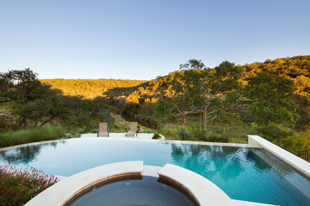 Design ideas for an expansive traditional back custom shaped infinity hot tub in Austin with natural stone paving.
