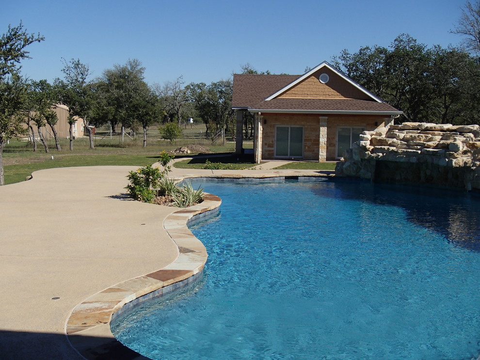 Inspiration for a rustic back custom shaped natural swimming pool in Austin with a water feature and stamped concrete.