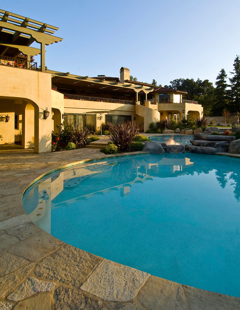 Ejemplo de piscina con fuente natural mediterránea grande a medida en patio trasero con adoquines de piedra natural