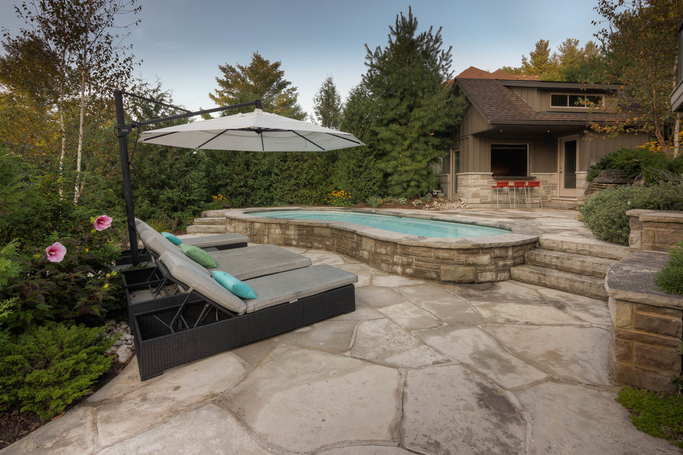 Medium sized traditional back kidney-shaped swimming pool in Toronto with a pool house and natural stone paving.