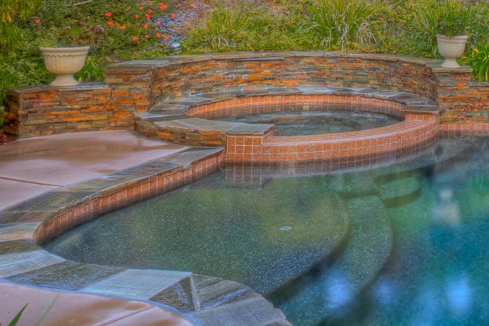 Esempio di una piscina tradizionale personalizzata di medie dimensioni e dietro casa con una vasca idromassaggio e lastre di cemento