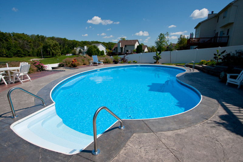 Ejemplo de casa de la piscina y piscina alargada clásica de tamaño medio tipo riñón en patio trasero con suelo de hormigón estampado