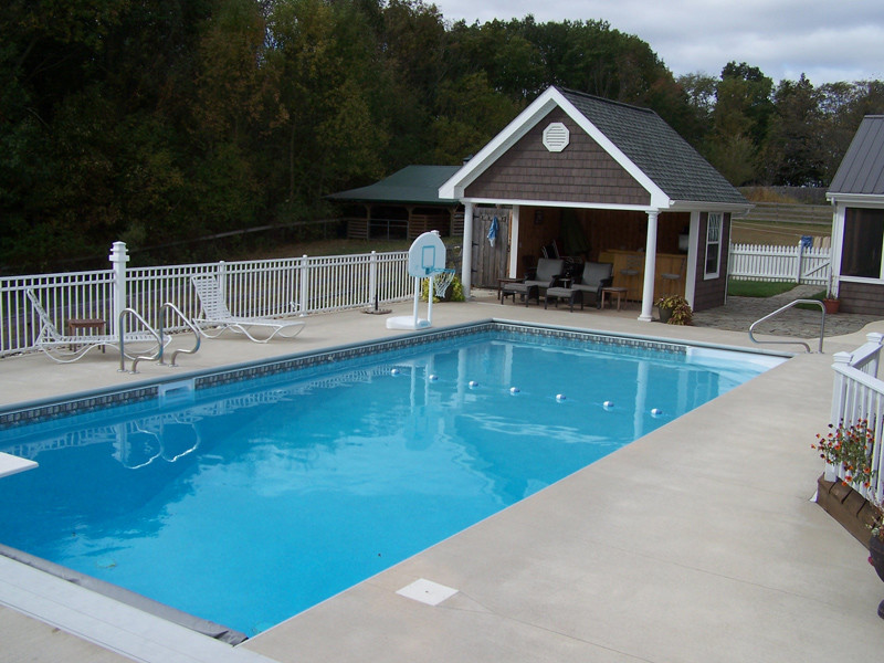 Modelo de casa de la piscina y piscina alargada clásica de tamaño medio rectangular en patio trasero con losas de hormigón