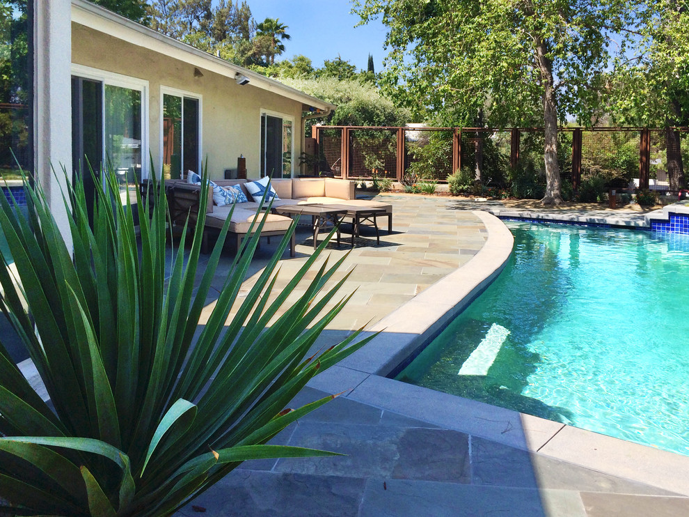 Foto på en stor funkis pool på baksidan av huset, med en fontän och naturstensplattor