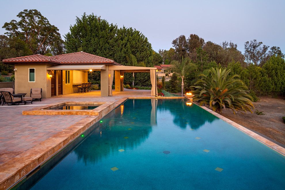 Diseño de piscina con fuente infinita actual grande rectangular en patio lateral con adoquines de ladrillo