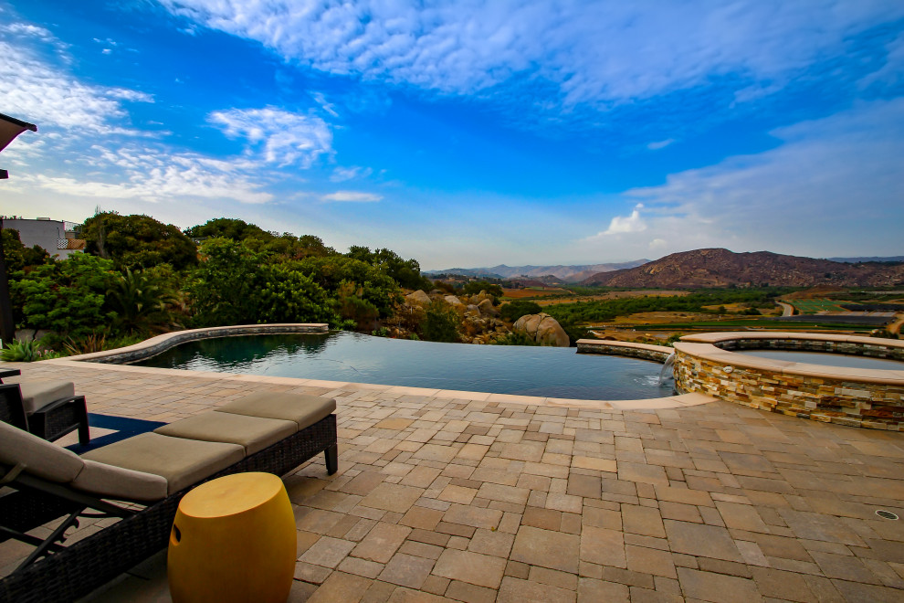 Inspiration for a medium sized mediterranean back custom shaped infinity swimming pool in San Diego with with pool landscaping and concrete paving.