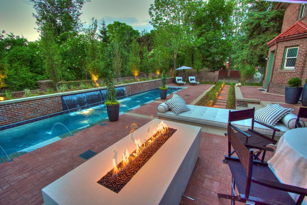 Diseño de piscina alargada moderna grande rectangular en patio trasero con adoquines de ladrillo