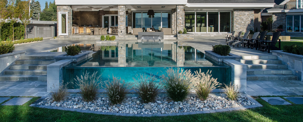 Foto di una piscina a sfioro infinito tradizionale rettangolare di medie dimensioni e davanti casa con fontane e pavimentazioni in pietra naturale