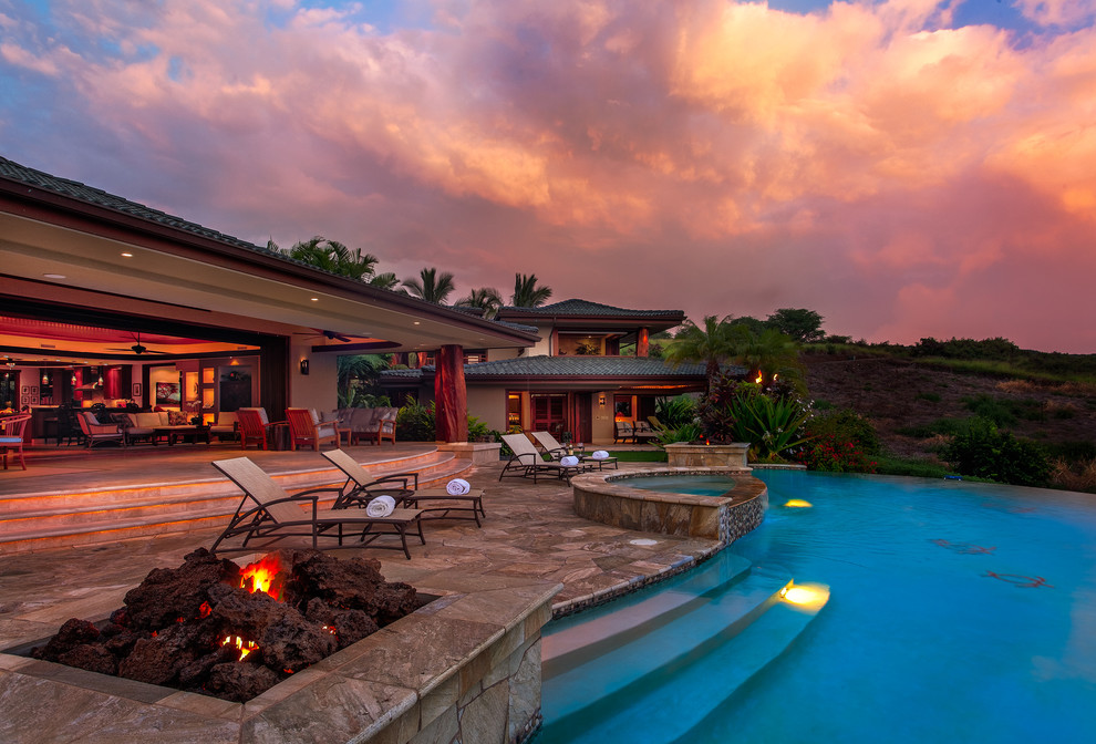 Esempio di una grande piscina a sfioro infinito tropicale personalizzata dietro casa con una vasca idromassaggio e pavimentazioni in pietra naturale