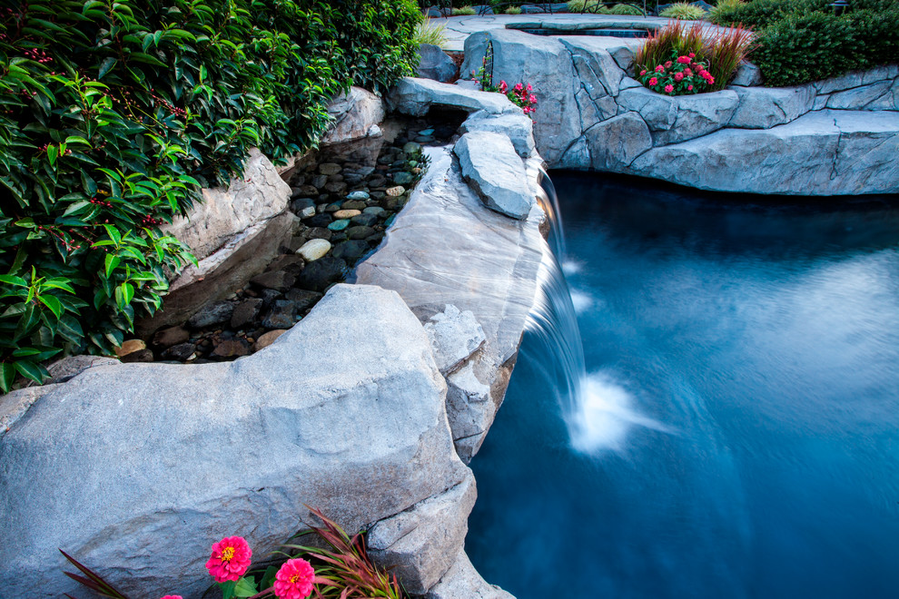 Immagine di una grande piscina country personalizzata dietro casa con fontane e cemento stampato