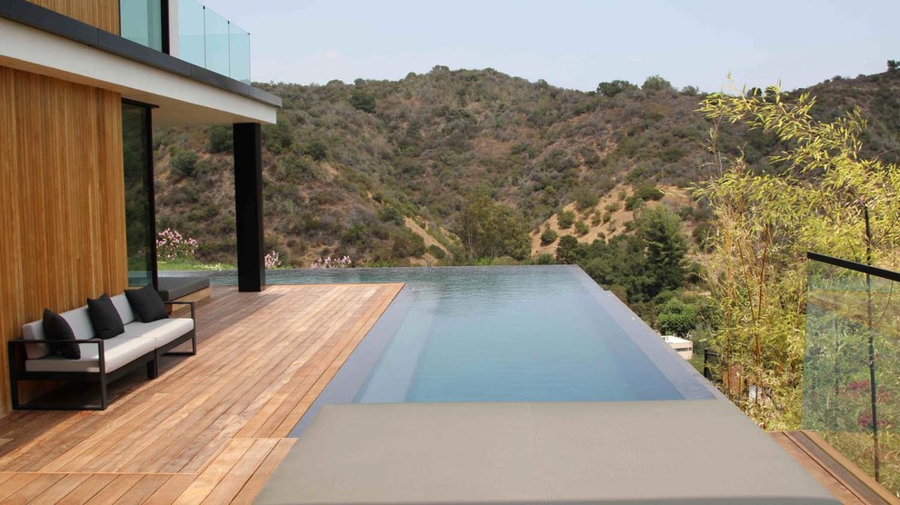 Cette photo montre une piscine à débordement et arrière tendance en L de taille moyenne avec une terrasse en bois.