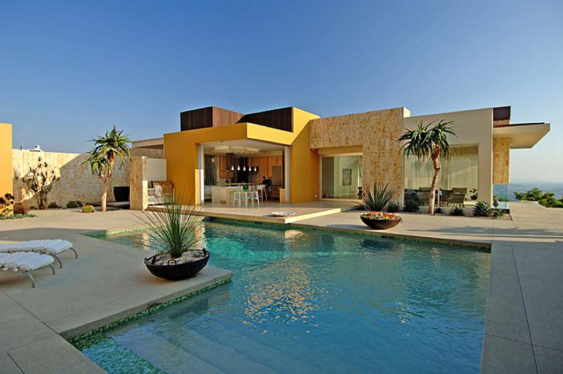 This is an example of a large contemporary back l-shaped infinity swimming pool in Los Angeles with a pool house and concrete slabs.
