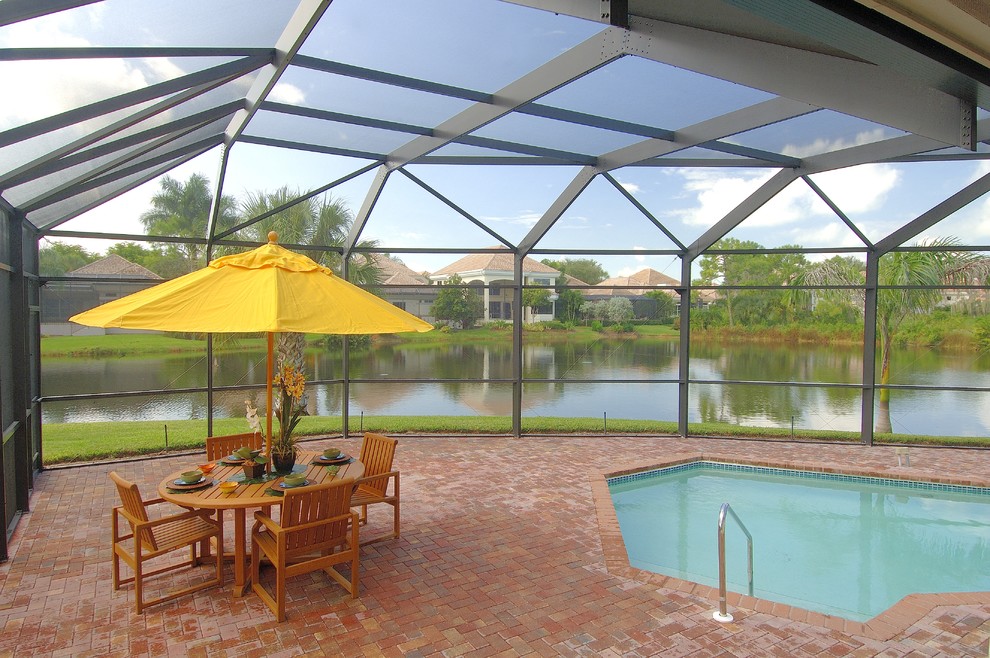 Modelo de piscina tropical grande en patio trasero con adoquines de ladrillo