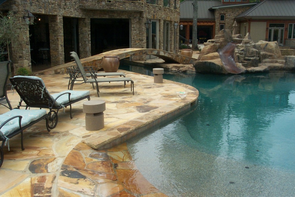 Modelo de piscina con tobogán natural rústica grande a medida en patio trasero con adoquines de piedra natural