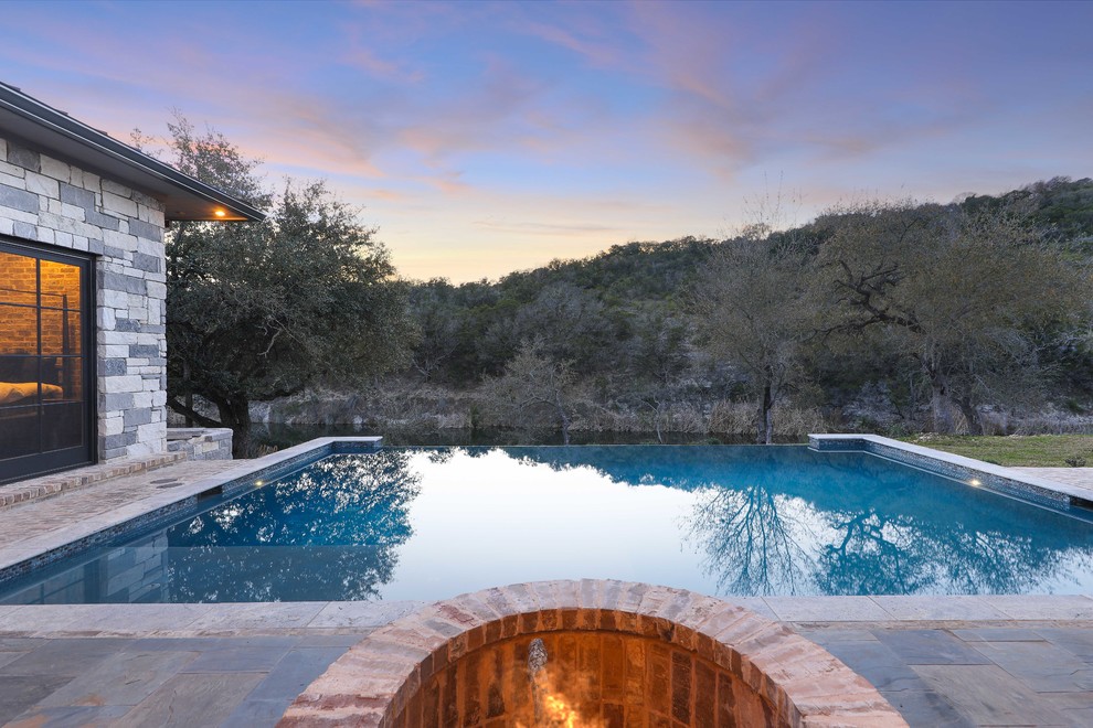 Example of a large trendy backyard brick and rectangular infinity pool fountain design in Austin