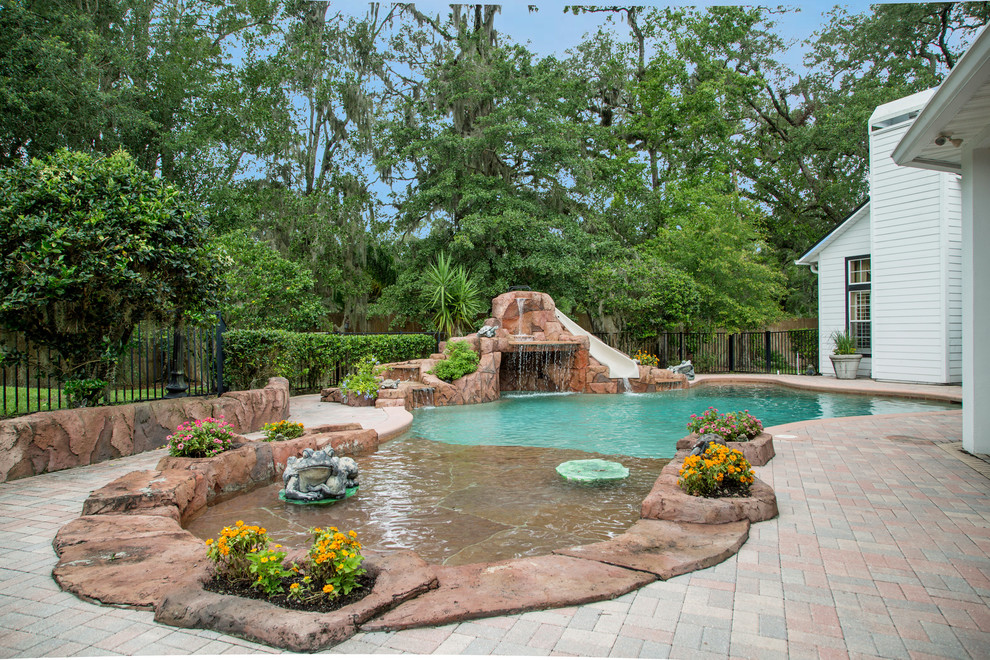 На фото: бассейн произвольной формы в классическом стиле с водной горкой и покрытием из каменной брусчатки с