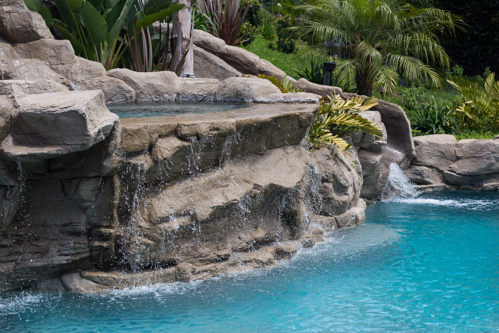 Ejemplo de piscina con tobogán natural de estilo americano grande a medida en patio trasero con adoquines de piedra natural