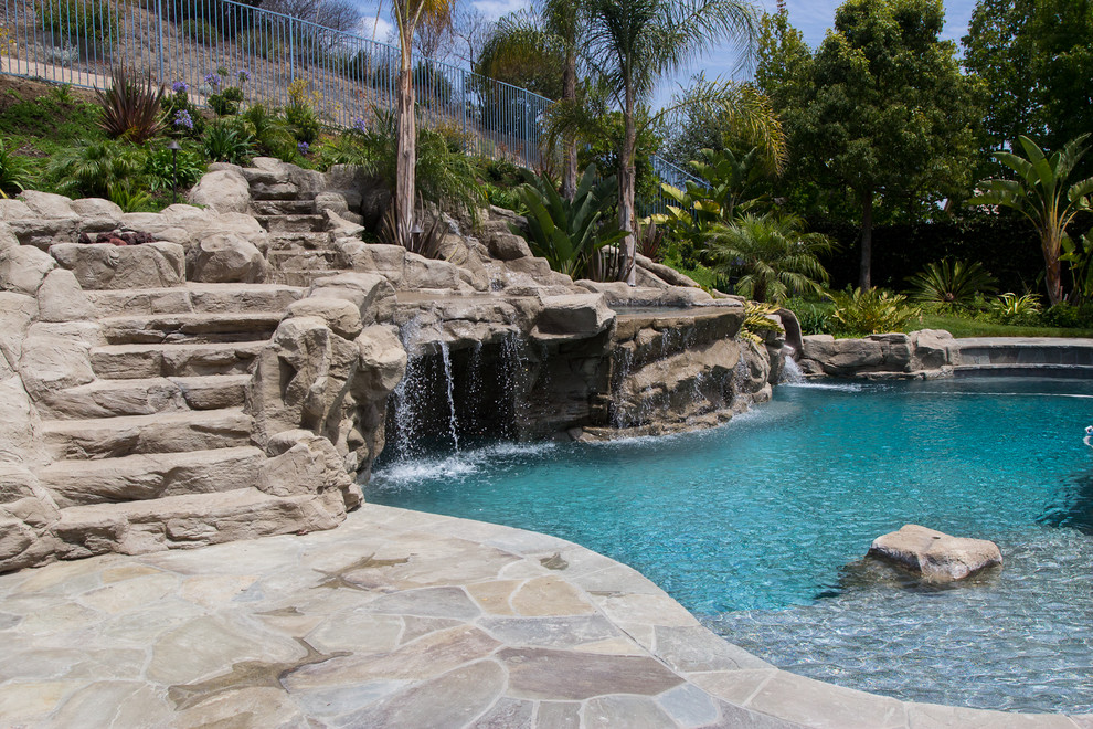 Ispirazione per una grande piscina naturale tropicale personalizzata dietro casa con un acquascivolo e pavimentazioni in pietra naturale