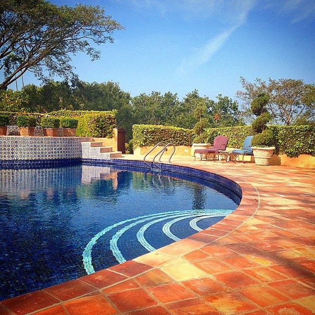 На фото: естественный, круглый бассейн на заднем дворе в средиземноморском стиле с домиком у бассейна и покрытием из плитки с
