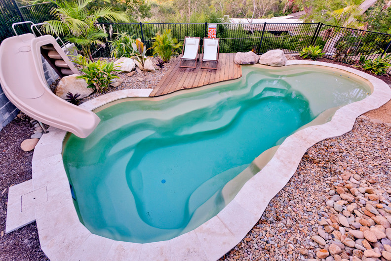 Modelo de piscina con tobogán natural marinera grande a medida en patio trasero con gravilla