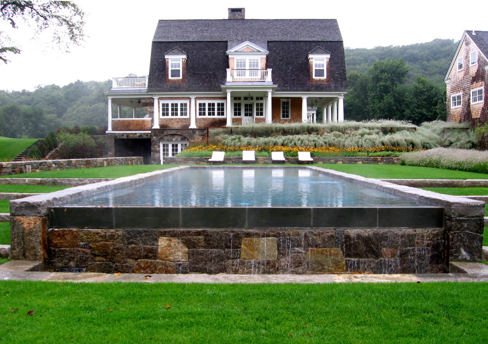 Diseño de piscina infinita de estilo de casa de campo rectangular en patio trasero con adoquines de piedra natural