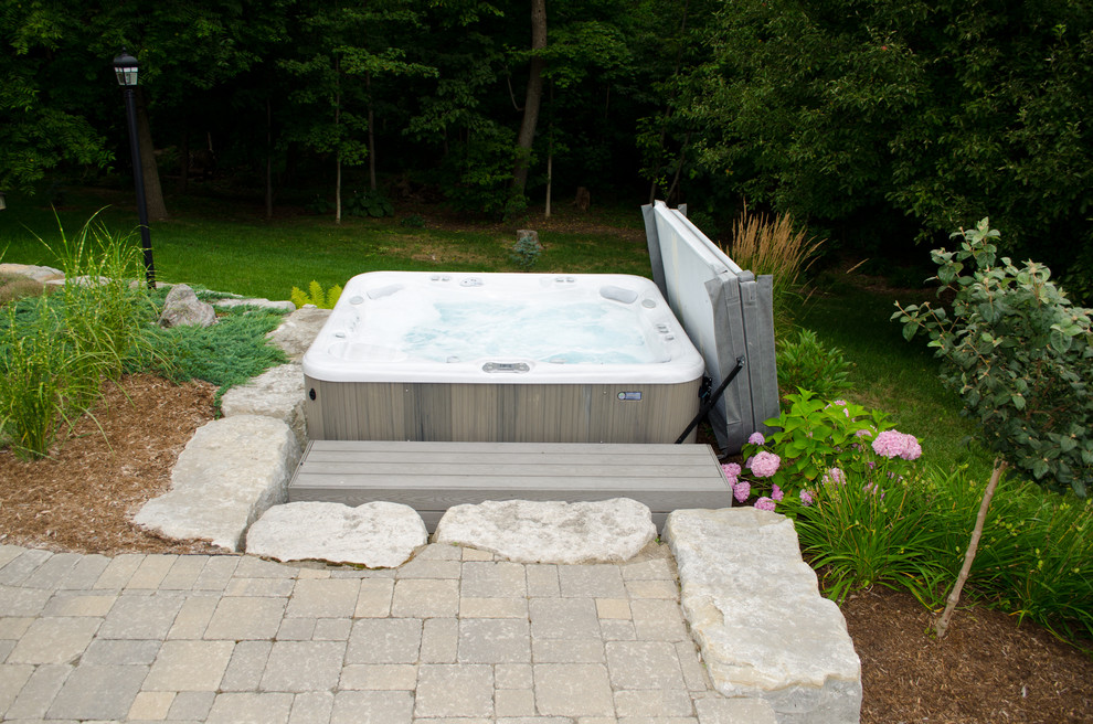 Modelo de piscinas y jacuzzis elevados clásicos de tamaño medio en patio trasero con adoquines de hormigón