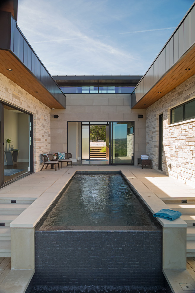 Ejemplo de piscina infinita contemporánea de tamaño medio a medida en patio con adoquines de hormigón