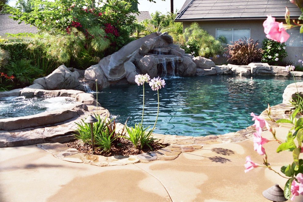 Ispirazione per una piscina naturale tropicale personalizzata di medie dimensioni e dietro casa con un acquascivolo e lastre di cemento