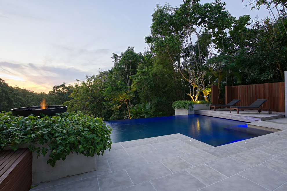 Ispirazione per una grande piscina a sfioro infinito tropicale rettangolare dietro casa con pavimentazioni in pietra naturale