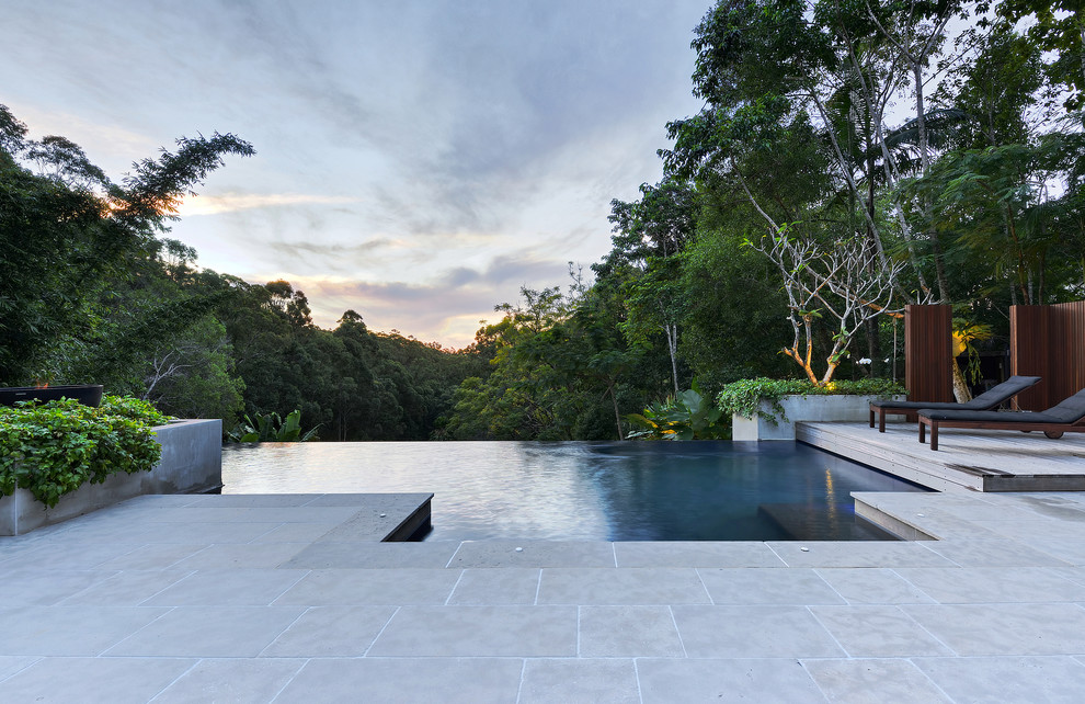 Foto på en stor tropisk infinitypool på baksidan av huset, med naturstensplattor