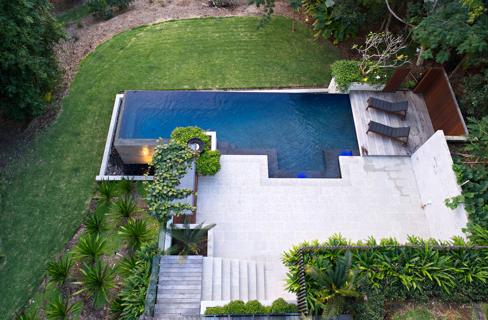 На фото: большой прямоугольный бассейн-инфинити на заднем дворе в морском стиле с покрытием из каменной брусчатки