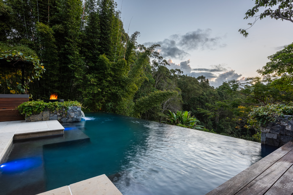 Esempio di una grande piscina a sfioro infinito tropicale personalizzata dietro casa con una dépendance a bordo piscina e pavimentazioni in pietra naturale