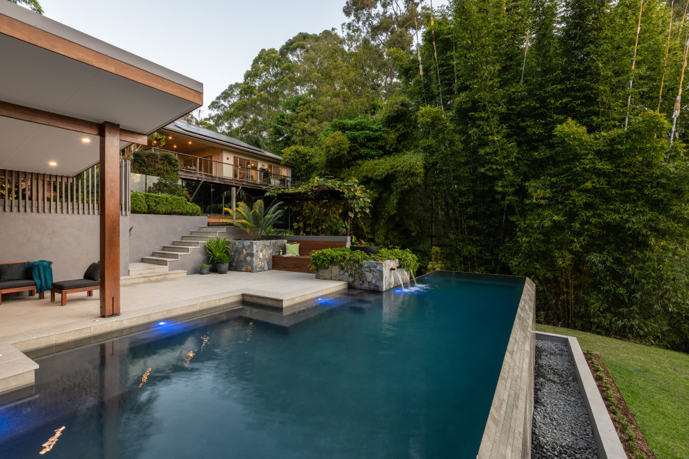 Ispirazione per una grande piscina a sfioro infinito tropicale personalizzata dietro casa con una dépendance a bordo piscina e pavimentazioni in pietra naturale
