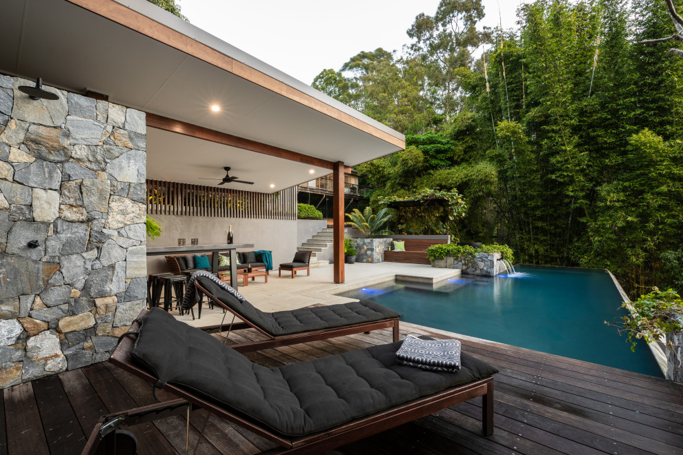 Foto på en stor tropisk infinitypool på baksidan av huset, med poolhus och naturstensplattor