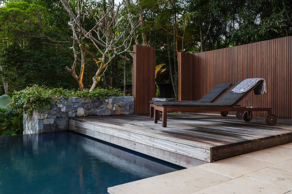 Cette photo montre une grande piscine à débordement et arrière exotique avec une terrasse en bois.