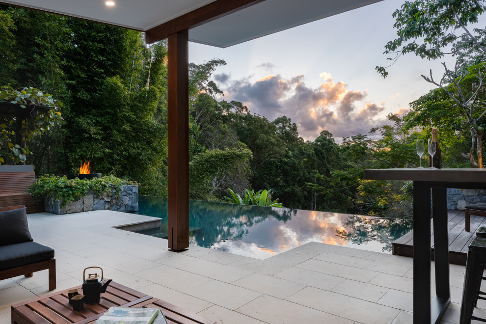 Ejemplo de casa de la piscina y piscina infinita tropical grande a medida en patio trasero con adoquines de piedra natural