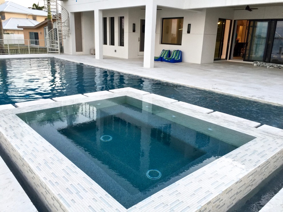 Esempio di una grande piscina a sfioro infinito tropicale rettangolare dietro casa con una vasca idromassaggio e piastrelle