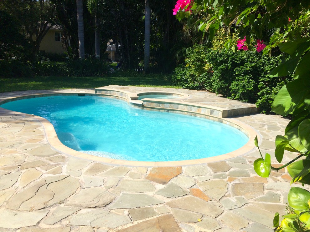 Bild på en mellanstor tropisk anpassad pool på baksidan av huset, med spabad och naturstensplattor