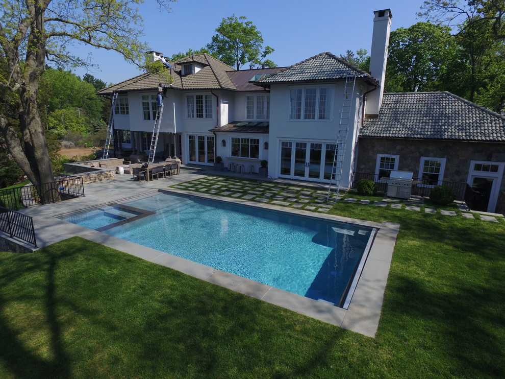 Diseño de piscina contemporánea grande rectangular en patio trasero con adoquines de piedra natural