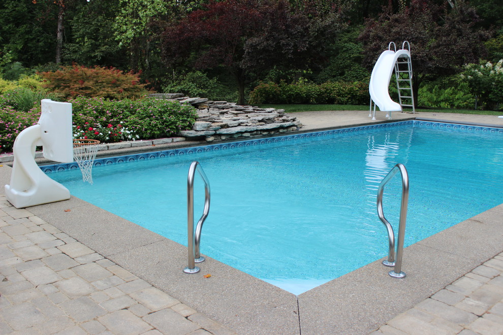 На фото: большой прямоугольный бассейн на заднем дворе в современном стиле с водной горкой и покрытием из каменной брусчатки с