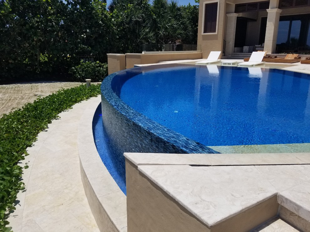 На фото: большой бассейн-инфинити произвольной формы на заднем дворе в средиземноморском стиле с покрытием из плитки с