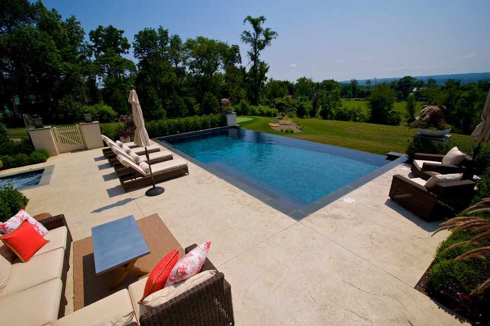 Diseño de piscina con fuente infinita actual grande rectangular en patio trasero con suelo de hormigón estampado