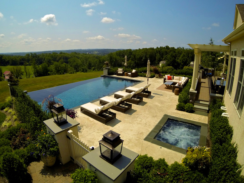 Diseño de piscina con fuente infinita contemporánea grande rectangular en patio trasero con suelo de hormigón estampado