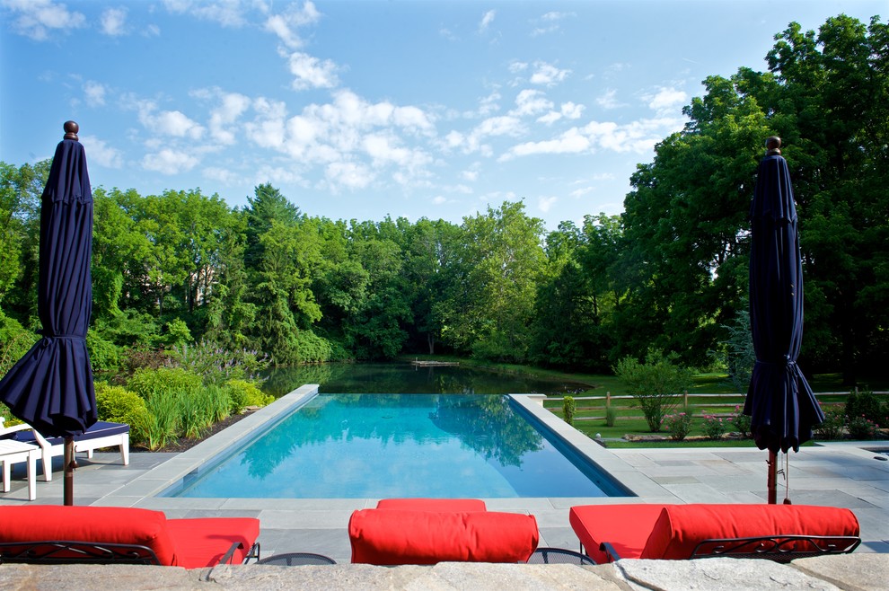 Aménagement d'une grande piscine à débordement et arrière classique rectangle avec un point d'eau et des pavés en pierre naturelle.