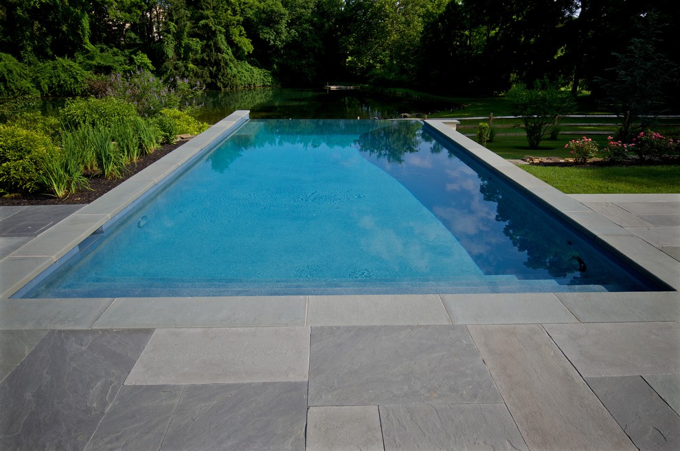 Esempio di una grande piscina a sfioro infinito chic rettangolare dietro casa con fontane e pavimentazioni in pietra naturale