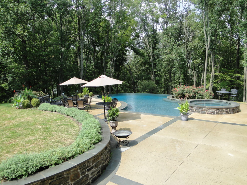 Large contemporary back custom shaped infinity swimming pool in Philadelphia with a water feature and concrete slabs.